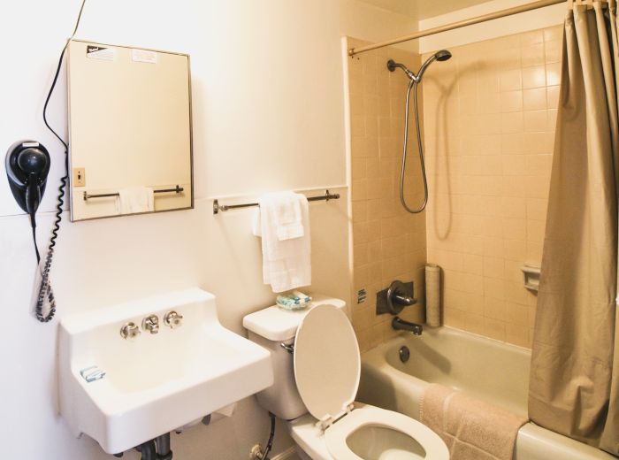A bathroom with a sink, mirror cabinet, toilet, bathtub with shower, towels, and a wall-mounted hairdryer.