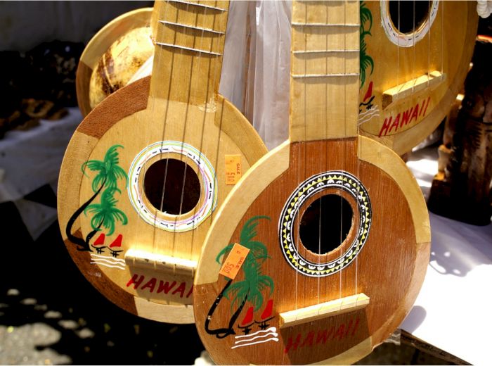 The image shows three small wooden guitars with tropical decorations and the word "HAWAII" on them, hanging on display.
