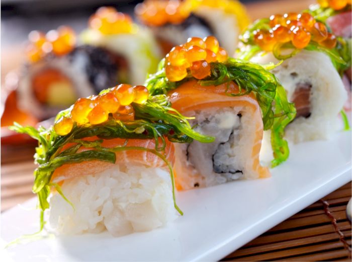 The image shows a plate of sushi rolls topped with seaweed and fish roe, arranged on a bamboo mat.