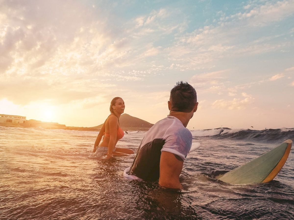 Two people are sitting on surfboards in the ocean at sunset, enjoying the waves.