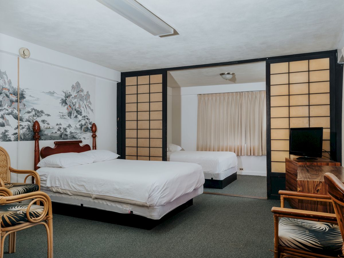 The image shows a spacious room with two double beds, bamboo chairs, a TV on a wooden stand, and a large art piece on the wall.